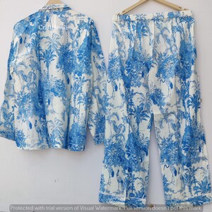 May include: A white pajama set with a blue and white tropical print featuring palm trees and birds. The set includes a long-sleeved shirt and pants.