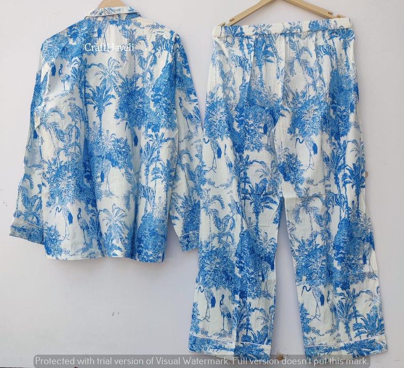 May include: A white pajama set with a blue and white tropical print featuring palm trees and birds. The set includes a long-sleeved shirt and pants.