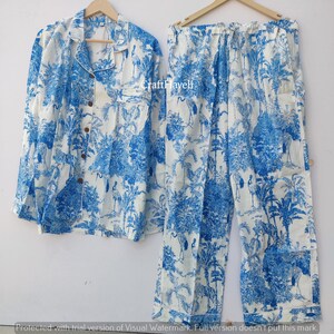 May include: A white and blue pajama set with a crane and palm tree print. The set includes a long-sleeved shirt with a button-up front and matching pants.