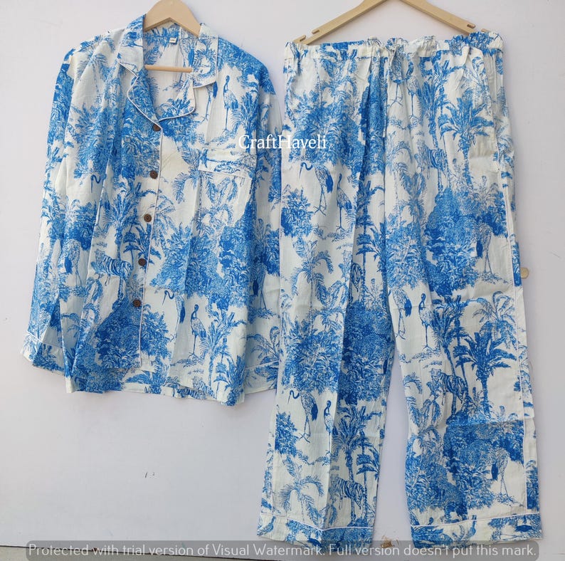 May include: A white and blue pajama set with a crane and palm tree print. The set includes a long-sleeved shirt with a button-up front and matching pants.