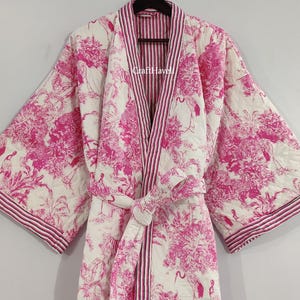 May include: A white and pink quilted robe with a floral print and a striped inner lining. The robe has a sash tie and long sleeves. The text "Craft Havel" is visible on the robe.