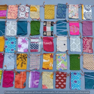 以下が含まれることがあります： 様々なカラフルな模様が施された、小さな布製の巾着袋が36個集められています。袋は薄い青色の表面にグリッド状に並べられています。画像の中央には「Craft Haveli」という文字が見えます。