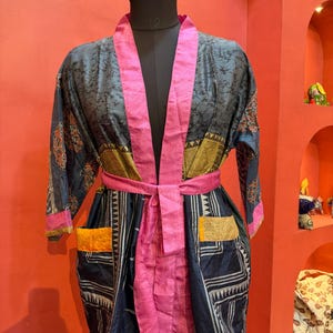 Może przedstawiać: Wzorzysty szlafrok w stylu kimono w odcieniach niebieskiego, różowego i złotego, prezentowany na manekinie. Szlafrok posiada różowy pas, kieszenie i wykończenia. Tkanina ma szczegółowy wzór.