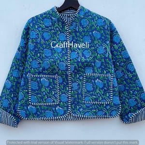Könnte beinhalten: Eine blaue gesteppte Jacke mit Blumenmuster und weißem Besatz. Die Jacke hat einen Stehkragen und zwei Taschen. Der Text "Craft Haveli" ist auf der Vorderseite der Jacke aufgedruckt.