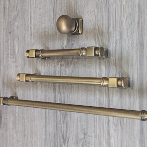 May include: Three antique brass cabinet pulls with square ends and a round knob. The pulls are arranged in a vertical line, with the knob at the top.