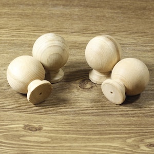 May include: Four wooden knobs with a round shape and a small base. The knobs are light brown in color and are arranged in a circle on a wooden surface.