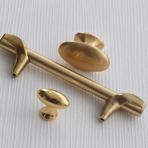 May include: Three gold-toned cabinet knobs. Two are round and one is a long, thin bar with curved ends.