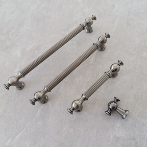 Puede incluir: Cuatro tiradores de armario plateados con un diseño acanalado. Los tiradores son de diferentes tamaños, siendo el más grande de unos 15 cm de largo. El tirador más pequeño es un pomo redondo.