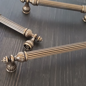 May include: Three antique-style cabinet door pulls with a fluted design and ornate metal knobs. The pulls are made of a brushed metal finish.