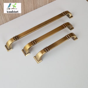 May include: Three antique brass cabinet pulls in different sizes. The pulls have a square base and a curved top with decorative grooves.