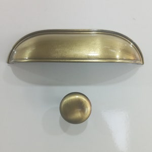 May include: A set of two gold-toned cabinet hardware pieces. The first piece is a curved, arched pull handle. The second piece is a round knob.