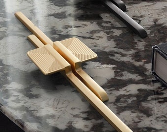 May include: Two cabinet door pulls, one gold and one black, with a geometric design. The pulls are made of metal and have a sleek, modern look.