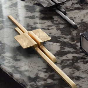 May include: Two cabinet door pulls, one gold and one black, with a geometric design. The pulls are made of metal and have a sleek, modern look.