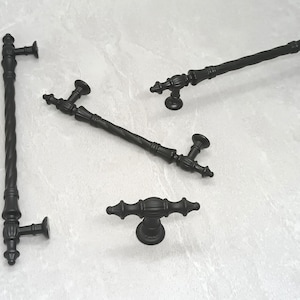 May include: Four black metal cabinet pulls with different styles.  The pulls are on a white background.