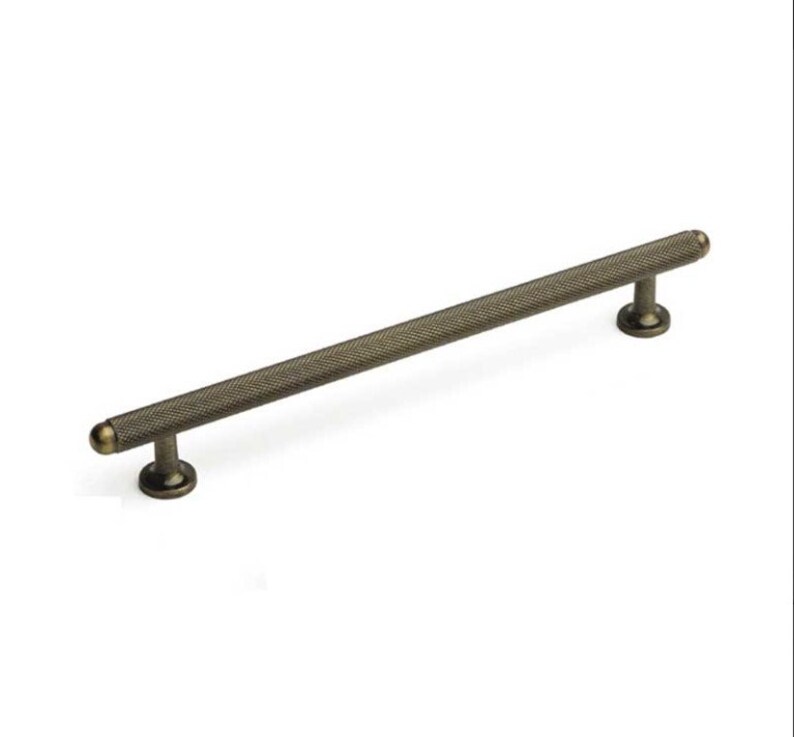 May include: A long, antique brass cabinet pull with a textured, diamond-shaped pattern. The pull has rounded ends.