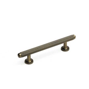 May include: A brushed antique brass cabinet pull with a textured cylindrical design. The pull has rounded ends and a simple, modern style.