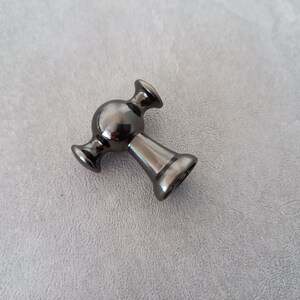 May include: A black metal cabinet knob with a round, spherical design and two side arms.