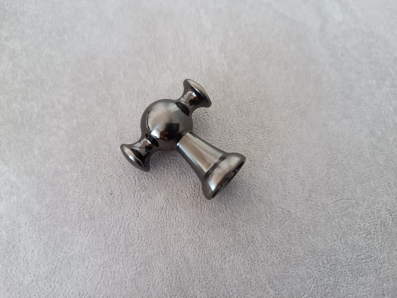 May include: A black metal cabinet knob with a round, spherical design and two side arms.