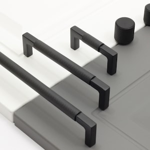 Puede incluir: Una colección de herrajes negros para gabinetes, que incluye dos tiradores largos de barra, dos tiradores más cortos y dos perillas redondas. Los tiradores y las perillas tienen un agarre texturizado con patrón de diamante.