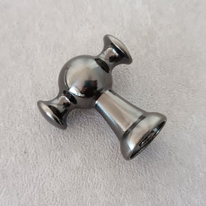 May include: A black metal cabinet knob with a round, spherical design and two arms extending out from the sides.