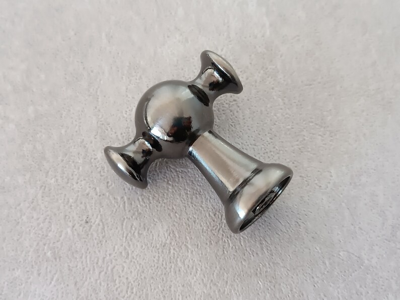 May include: A black metal cabinet knob with a round, spherical design and two arms extending out from the sides.