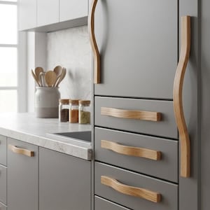 Puede incluir: Una cocina moderna con gabinetes grises y tiradores de cajones de madera clara. Los gabinetes tienen un diseño minimalista, con manijas largas y curvas de madera en los gabinetes altos y tiradores más cortos en forma de onda en los cajones.