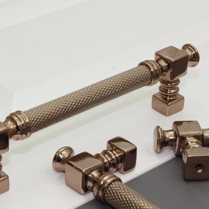 May include: Three rose gold cabinet pulls with a square base and a textured, cylindrical handle.