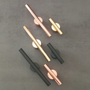 Può includere: Tre set di ferramenta per mobili con un design moderno. Ogni set presenta una barra dritta con un pomo rotondo a ciascuna estremità. I set sono in nero, oro rosa e oro.