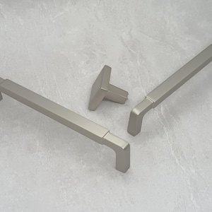 May include: Three silver cabinet pulls, two are long and rectangular with rounded edges, one is a small square knob with a rounded top.