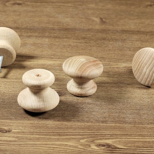 May include: Four wooden cabinet knobs with a natural finish. The knobs are different shapes and sizes.