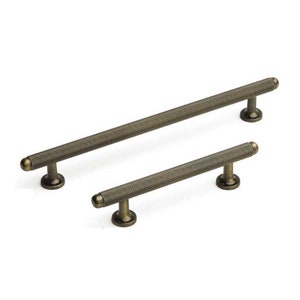 May include: Two antique brass cabinet pulls with a textured finish. The larger pull is approximately 15cm long and the smaller pull is approximately 10cm long.
