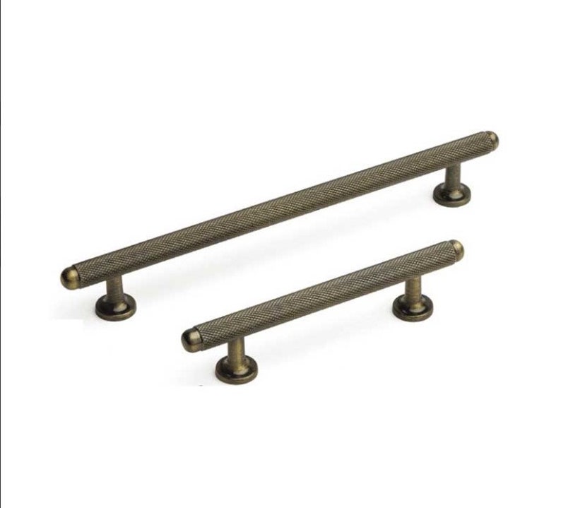 May include: Two antique brass cabinet pulls with a textured finish. The larger pull is approximately 15cm long and the smaller pull is approximately 10cm long.