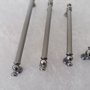 May include: Four silver cabinet pulls with a fluted design and round knobs. The pulls are arranged in a row on a light grey surface.