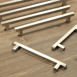 May include: Five silver cabinet pulls with a brushed finish. The pulls are arranged in a row, with the largest pull at the bottom and the smallest pull at the top. The pulls are all rectangular in shape and have a slight curve at the top.