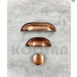 Könnte beinhalten: Drei kupferne Schrankgriffe in verschiedenen Größen. Der größte Griff ist halbkreisförmig, der mittlere Griff ist halbkreisförmig und der kleinste Griff ist ein runder Knopf.