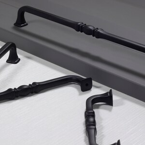 Può includere: Quattro maniglie per armadi in metallo nero con un design ornamentale. Le maniglie sono di diverse dimensioni e forme.