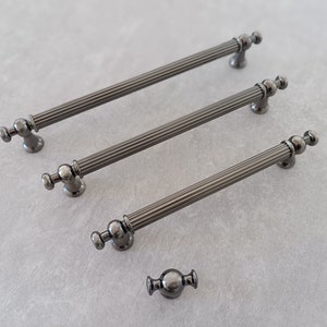 May include: Three black metal cabinet pulls with fluted detailing and round knobs. A smaller black metal knob with a round design is also shown.
