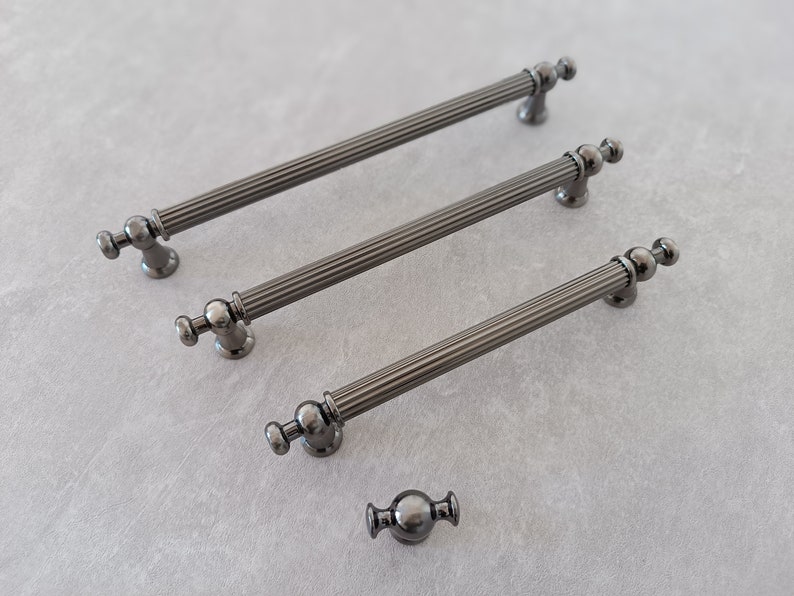 May include: Three black metal cabinet pulls with fluted detailing and round knobs. A smaller black metal knob with a round design is also shown.