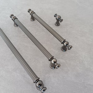 May include: Three black metal cabinet pulls with a fluted design and round knobs. The pulls are arranged in a row from longest to shortest.