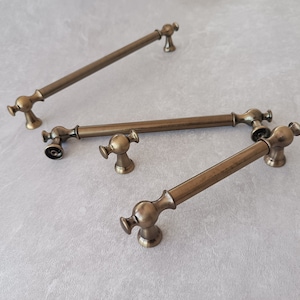 May include: Three antique brass cabinet pulls with different styles. The pulls are all made of metal and have a distressed finish.