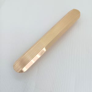 Può includere: Una maniglia per armadio in metallo color oro con una texture rigata.