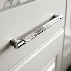 May include: A silver cabinet pull with a textured, diamond-patterned center and square end mounts. The handle is mounted on a white cabinet door. This modern hardware adds a touch of elegance to any kitchen or bathroom.