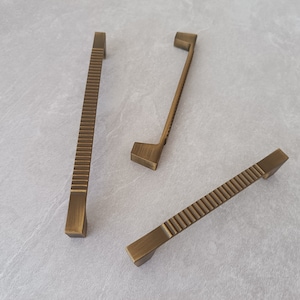 May include: Three antique gold cabinet pulls with a textured, ribbed design. The pulls are in various sizes and shapes.