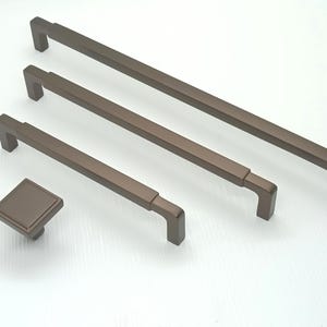 May include: Four bronze cabinet pulls in different sizes, with a square knob in the bottom left corner.