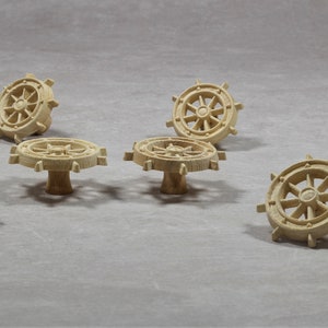 Pode incluir: Seis puxadores de gaveta de madeira em forma de rodas de navio. Os puxadores são de madeira castanho claro e têm um design simples.
