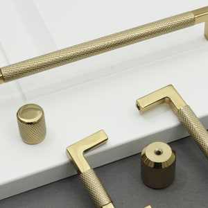 Könnte beinhalten: Ein Satz von vier goldenen Schrankknöpfen und -griffen mit einem strukturierten Diamantenmuster. Die Knöpfe sind rund und die Griffe sind rechteckig mit einem 90-Grad-Winkel.