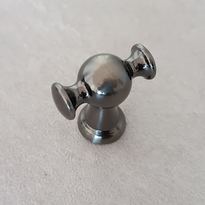 May include: A black metal cabinet knob with a round, spherical design and two arms extending out from the sides.