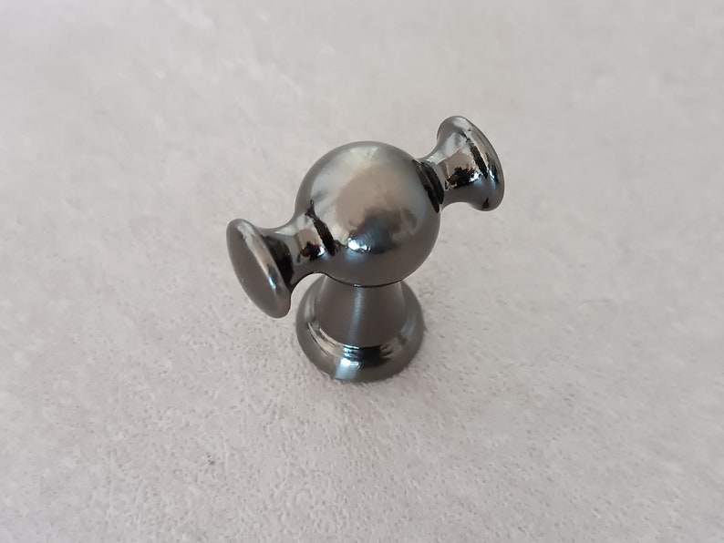 May include: A black metal cabinet knob with a round, spherical design and two arms extending out from the sides.