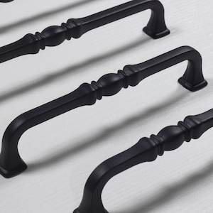 May include: Three black metal cabinet pulls with a decorative design. The pulls have a rounded center and a square end.
