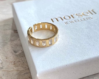 May include: Gold ring with a row of clear rectangular stones. The ring is on a white box with the text "morself jewellery".